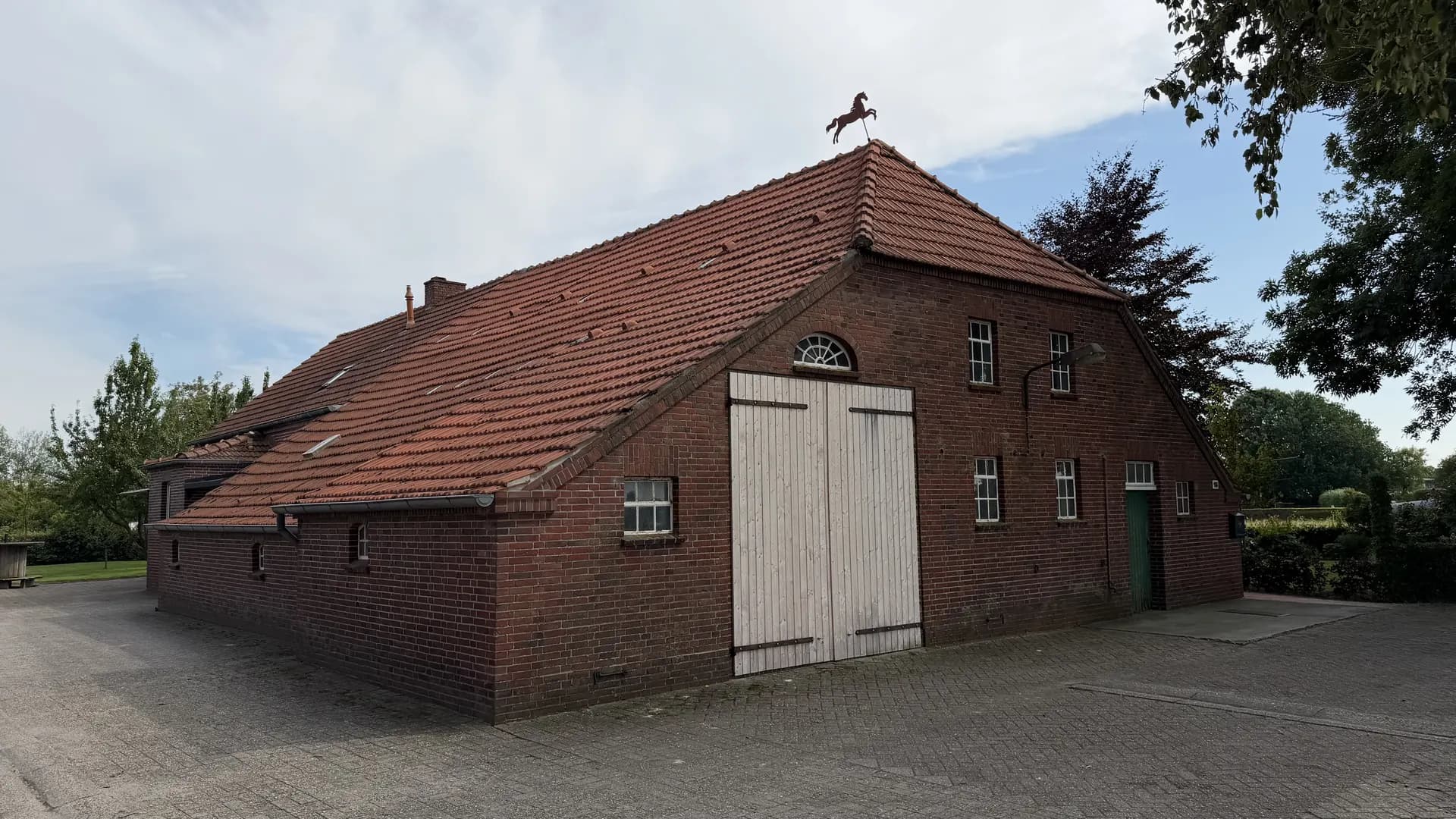 Backstein-Bauernhof mit Pferde-Wetterfahne und gepflasterter Hoffläche in Ostfriesland